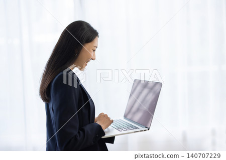 A young Japanese businesswoman is using her laptop by the window. 140707229