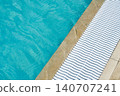 The edge of a natural stone pool with crystal clear blue water and a white plastic drain grate.  140707241