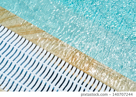 The edge of a pool with blue water and a white plastic drain grate.  140707244