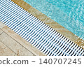The marble edge of the pool with crystal-clear blue water and a white plastic drain grate. 140707245