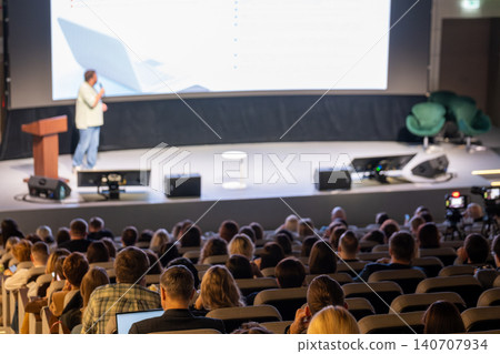 Presenter delivering business presentation on stage to large audience at conference auditorium Presenter delivering business presentation on stage to large audience at conference auditorium 140707934