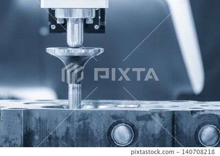 Close-up of an industrial robotic arm assembling intake and exhaust valves on a car engine cylinder head. 140708218