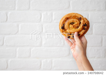Hand Holding Raisin Danish Pastry Against White Brick Wall Hand Holding Raisin Danish Pastry Against White Brick Wall 140708642