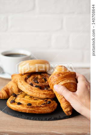 Hand Taking Croissant From Assortment of Fresh Pastries and Coffee Hand Taking Croissant From Assortment of Fresh Pastries and Coffee 140708644