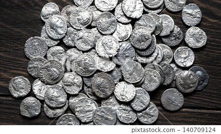 Collection of ancient Roman silver coins on a dark wooden table. Pile of authentic denarii with portraits of emperors, top view, for antique vintage background Collection of ancient Roman silver coins on a dark wooden table. Pile of authentic denarii with portraits of emperors, top view, for antique vintage background 140709124