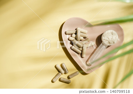 Collagen powder and supplement capsules in heart shaped dish on yellow background, wellness concept Collagen powder and supplement capsules in heart shaped dish on yellow background, wellness concept 140709518