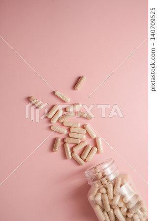 Collagen supplement capsules spilling from bottle on pink background with copy space, feminine food supplement abstract background 140709525