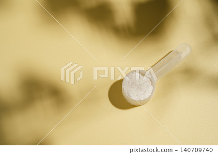 Collagen powder scoop on yellow background with sun light and dark shadows, food supplement concept Collagen powder scoop on yellow background with sun light and dark shadows, food supplement concept 140709740