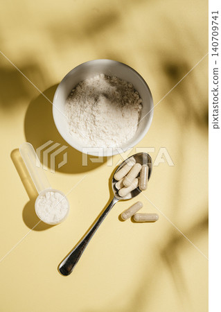 Collagen powder, capsules and scoop on yellow background with sun light and dark shadows, food supplement concept 140709741