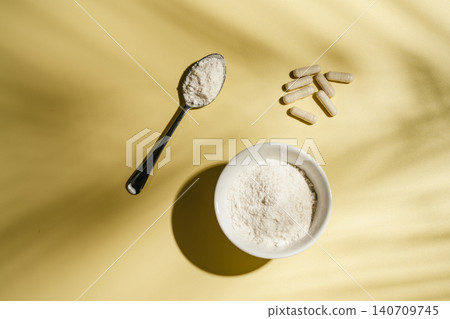 Collagen powder and dietary supplement capsules on yellow background with leaf shadows, flat lay 140709745