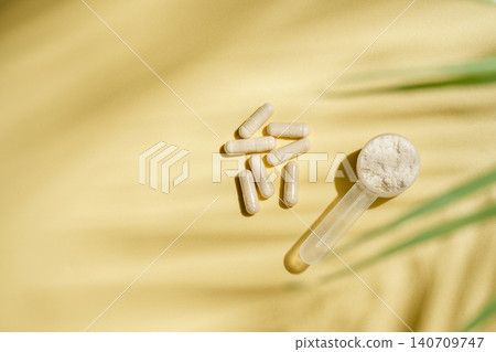 Collagen powder scoop and capsules on yellow background with copy space 140709747
