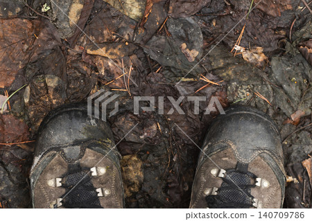 Worn hiking boots stand on a muddy forest floor, top view Worn hiking boots stand on a muddy forest floor, top view 140709786