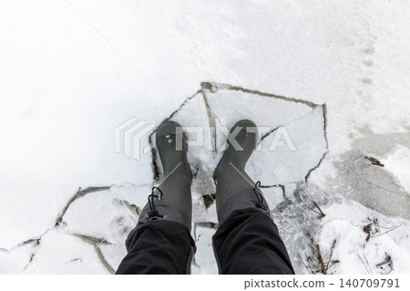 A top-down view of rubber boots standing on cracked ice A top-down view of rubber boots standing on cracked ice 140709791