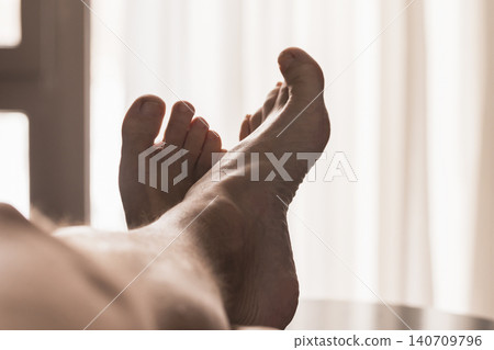 Bare feet stretched out on a bed in soft, warm morning light Bare feet stretched out on a bed in soft, warm morning light 140709796