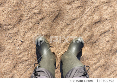 Top-down view of green rubber boots standing on fine sand Top-down view of green rubber boots standing on fine sand 140709798