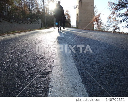 People walking uphill on asphalt road into sun 140709851