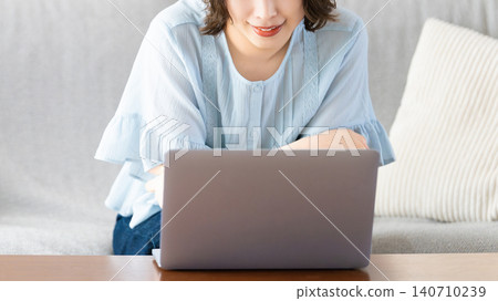 Woman sitting on a couch and using a computer Woman sitting on a couch and using a computer 140710239