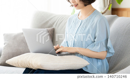 Woman sitting on a couch and using a computer Woman sitting on a couch and using a computer 140710246