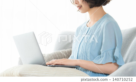 Woman sitting on a couch and using a computer 140710252