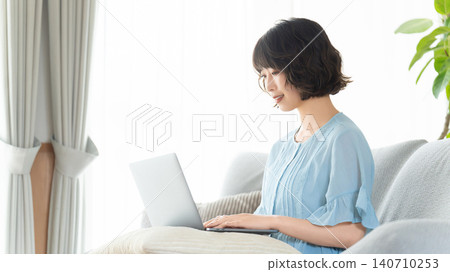 Woman sitting on a couch and using a computer Woman sitting on a couch and using a computer 140710253