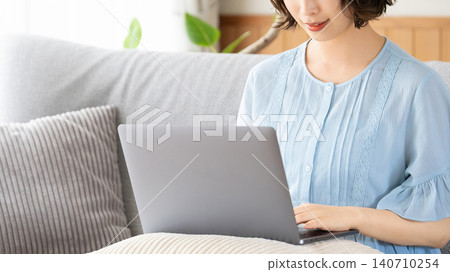 Woman sitting on a couch and using a computer Woman sitting on a couch and using a computer 140710254