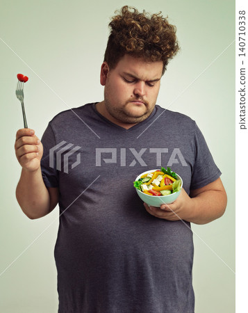 Unhappy, man and salad for diet with healthy food, fork or bowl and vegetables for wellness on studio background. Plus size person, fresh meal and lose weight for health, eating disorder or nutrition Unhappy, man and salad for diet with healthy food, fork or bowl and vegetables for wellness on studio background. Plus size person, fresh meal and lose weight for health, eating disorder or nutrition 140710338