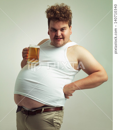 Obese, weight gain and lager for man in studio with drink for unhealthy habit, plus size and joke. Overweight person with glass on fat stomach for balance, drunk and humor for alcohol and comic 140710340