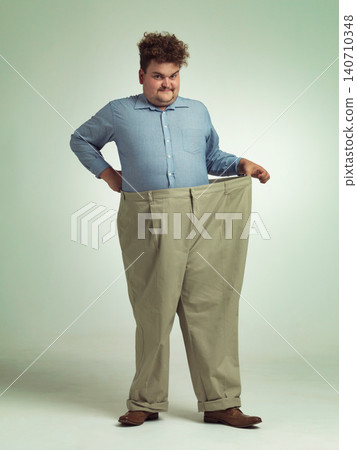 Happy man, portrait and plus size with pants for waist, weight loss or measurement on a studio background. Male person with smile for healthy diet, obesity or overweight clothing on mockup space Happy man, portrait and plus size with pants for waist, weight loss or measurement on a studio background. Male person with smile for healthy diet, obesity or overweight clothing on mockup space 140710348