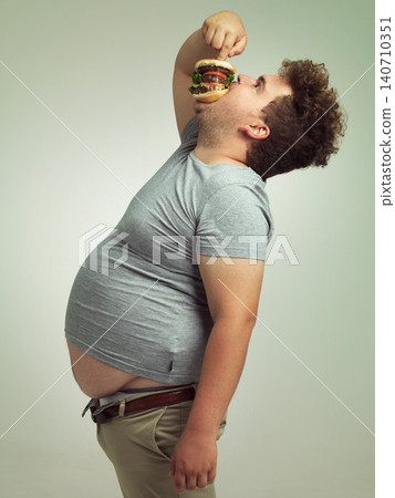 Fast food, hungry and man with hamburger in studio background with lunch, snack and craving for plus size guy. Male person, burger and takeaway for meal in mouth for eating, starving and bite Fast food, hungry and man with hamburger in studio background with lunch, snack and craving for plus size guy. Male person, burger and takeaway for meal in mouth for eating, starving and bite 140710351