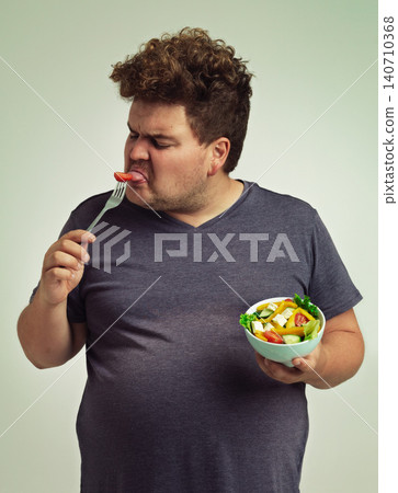 Man, salad and eating with disgust in studio for healthy diet, nutrition and unhappy for weight loss. Plus size, male person and fork with tomato for vitamin c, detox or organic food for lifestyle Man, salad and eating with disgust in studio for healthy diet, nutrition and unhappy for weight loss. Plus size, male person and fork with tomato for vitamin c, detox or organic food for lifestyle 140710368