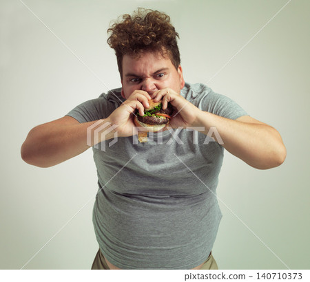 Takeaway, weight gain and burger for man in studio with fastfood for unhealthy eating, plus size and greed. Young person with meal in mouth and fat stomach for hunger, meat and sauce for bite indoor Takeaway, weight gain and burger for man in studio with fastfood for unhealthy eating, plus size and greed. Young person with meal in mouth and fat stomach for hunger, meat and sauce for bite indoor 140710373