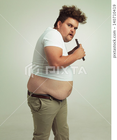Chocolate, portrait and plus size man with eating food, dessert and candy in a studio. Nutrition, sweet and unhealthy snack with sneaky and secret with a hungry male person with green background Chocolate, portrait and plus size man with eating food, dessert and candy in a studio. Nutrition, sweet and unhealthy snack with sneaky and secret with a hungry male person with green background 140710419