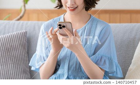 A woman sitting on a sofa in the living room and using a smartphone A woman sitting on a sofa in the living room and using a smartphone 140710457