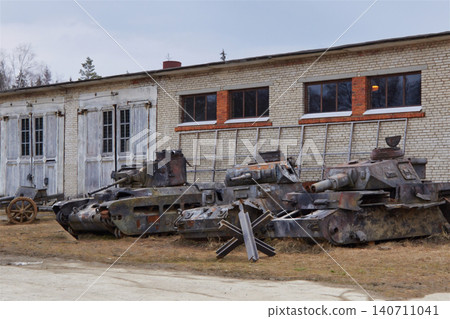 Abandoned rusted World War II tanks parked outside a brick military hangar during the day. Abandoned rusted World War II tanks parked outside a brick military hangar during the day. 140711041