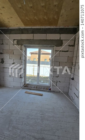 Unfinished room with concrete blocks and a white window looking out at a suburban house. 140711075