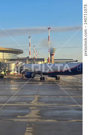 Commercial passenger airplane docked at a terminal boarding bridge under a clear morning sky. 140711078