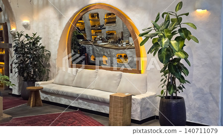 Modern luxury spa lounge features a white sofa, arched mirror, and green plants in a boutique. Modern luxury spa lounge features a white sofa, arched mirror, and green plants in a boutique. 140711079