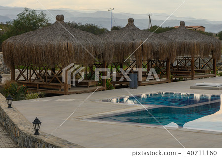 Relaxation huts near a sparkling pool surrounded by tranquil nature at dusk Relaxation huts near a sparkling pool surrounded by tranquil nature at dusk 140711160