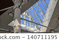 Modern architectural interior with white columns and large glass skylight under clear blue sky. 140711195