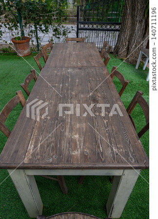 Long wooden table surrounded by chairs under lush greenery in a peaceful outdoor 140711196