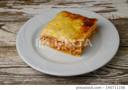 Delicious layers of cheesy lasagna served on a bright white plate against a rustic wooden background Delicious layers of cheesy lasagna served on a bright white plate against a rustic wooden background 140711198
