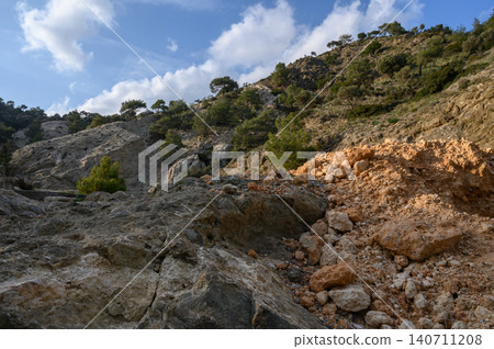 Rocky terrain under a bright blue sky with scattered clouds and lush greenery Rocky terrain under a bright blue sky with scattered clouds and lush greenery 140711208