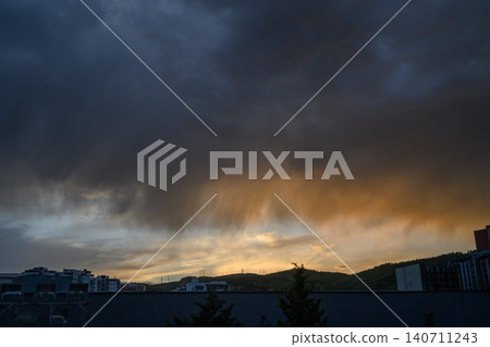 Dramatic sunset or sunrise over city with thick layer of dark storm clouds sunlight breaking through Dramatic sunset or sunrise over city with thick layer of dark storm clouds sunlight breaking through 140711243