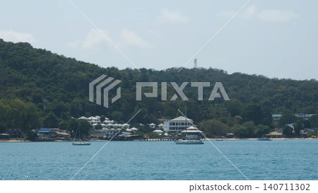 Panoramic view of Samet Island green hillside with buildings and calm turquoise sea in foreground from a ferry. Island scenery concept Panoramic view of Samet Island green hillside with buildings and calm turquoise sea in foreground from a ferry. Island scenery concept 140711302