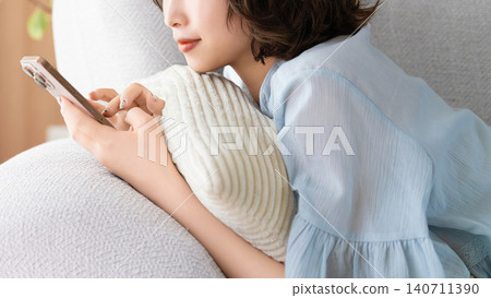 A woman lying on a sofa using a smartphone A woman lying on a sofa using a smartphone 140711390