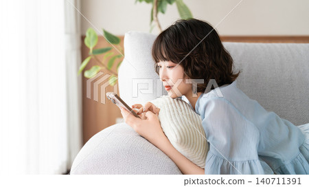 A woman lying on a sofa using a smartphone 140711391