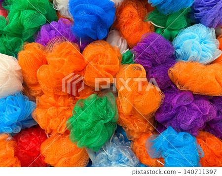 Colorful assortment of multicolored mesh bath sponge poufs piled together in a market 140711397