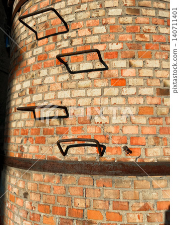 Close-up detail of curved old brick chimney surface with iron ladder rungs and horizontal metal band 140711401