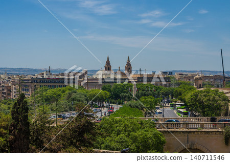 Panoramic Floriana Malta cityscape with St Publius Church twin towers dome green tree avenue limestone buildings and blue sky view 140711546