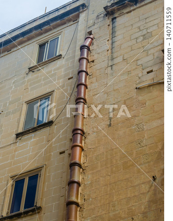 Traditional Maltese limestone building facade withold terracotta rainwater downpipe weathered stone wall and vintage windows Malta 140711559